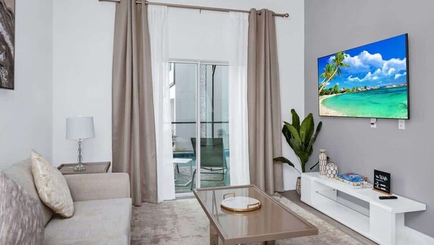 Un salon moderne avec un canapé, une table basse, un téléviseur et un balcon agrémenté de rideaux.
