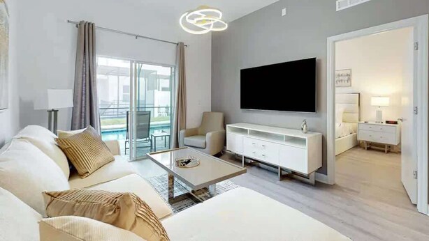 Un salón moderno con sofá, mesa de centro, televisor y vistas al exterior.