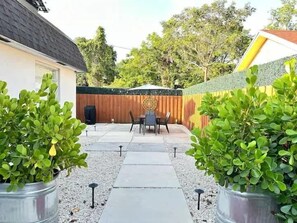 Un patio trasero con terraza, cerco de madera y plantas en macetas.