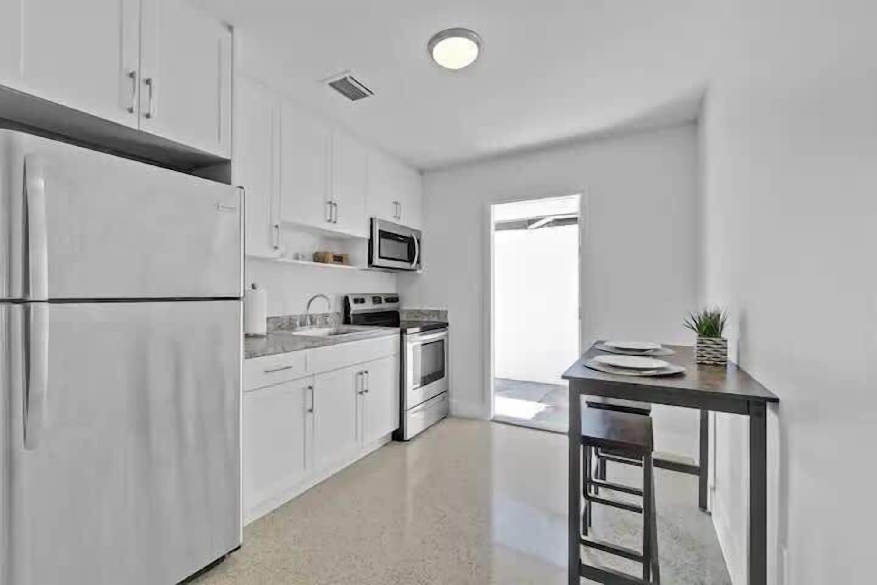 A modern kitchen with white cabinetry, stainless steel appliances, and a small dining area with a table and chairs.