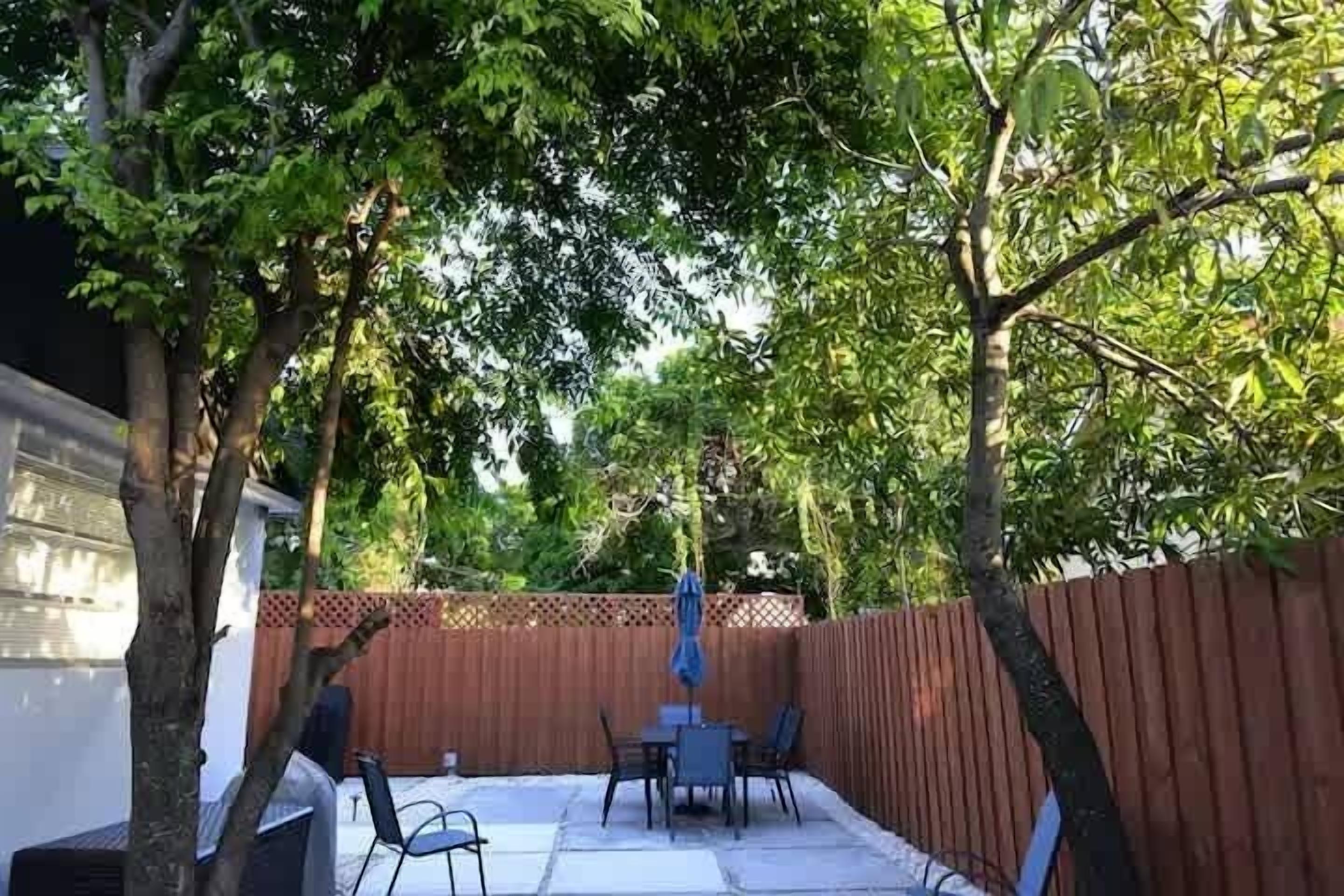 Een achtertuin met terras, een tafel en stoelen, omringd door een houten schutting en bomen.