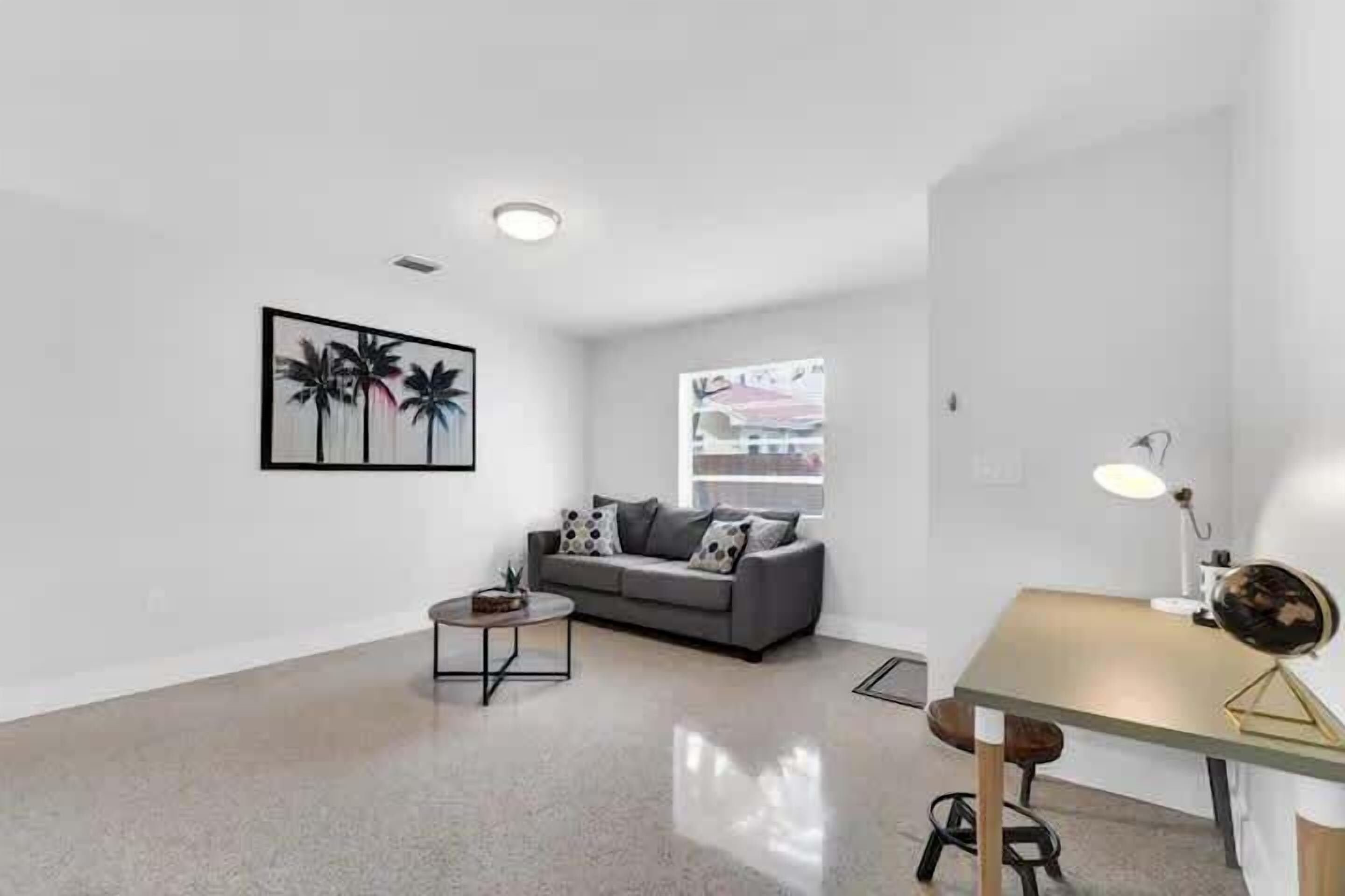 Un salon moderne avec un canapé gris, une petite table basse ronde et un bureau avec une lampe.