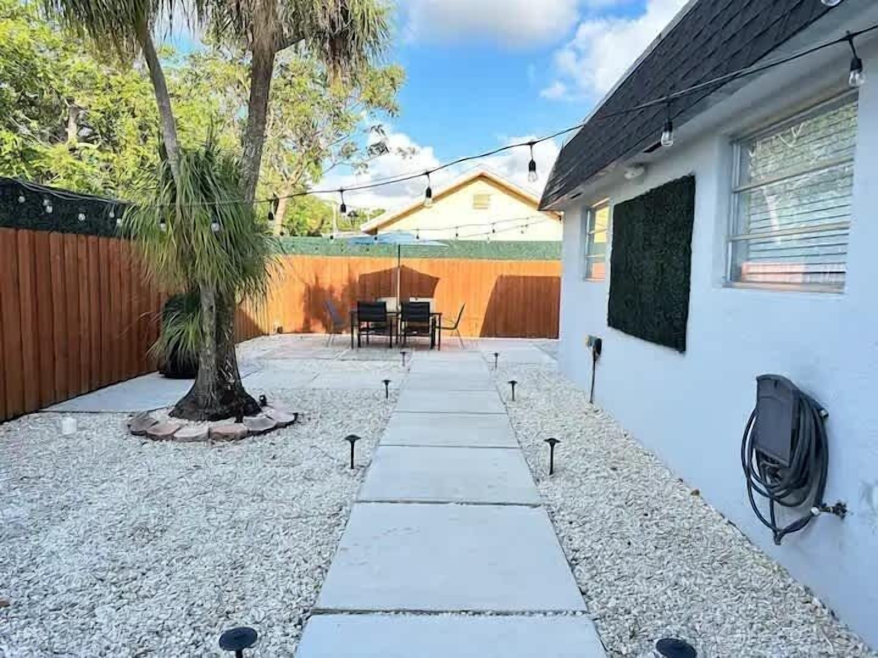A backyard with a patio, a wooden fence, a tree, and a house in the background.