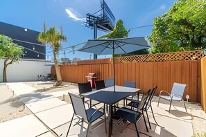 Un patio al aire libre con mesa y sillas, una valla de madera y un árbol.