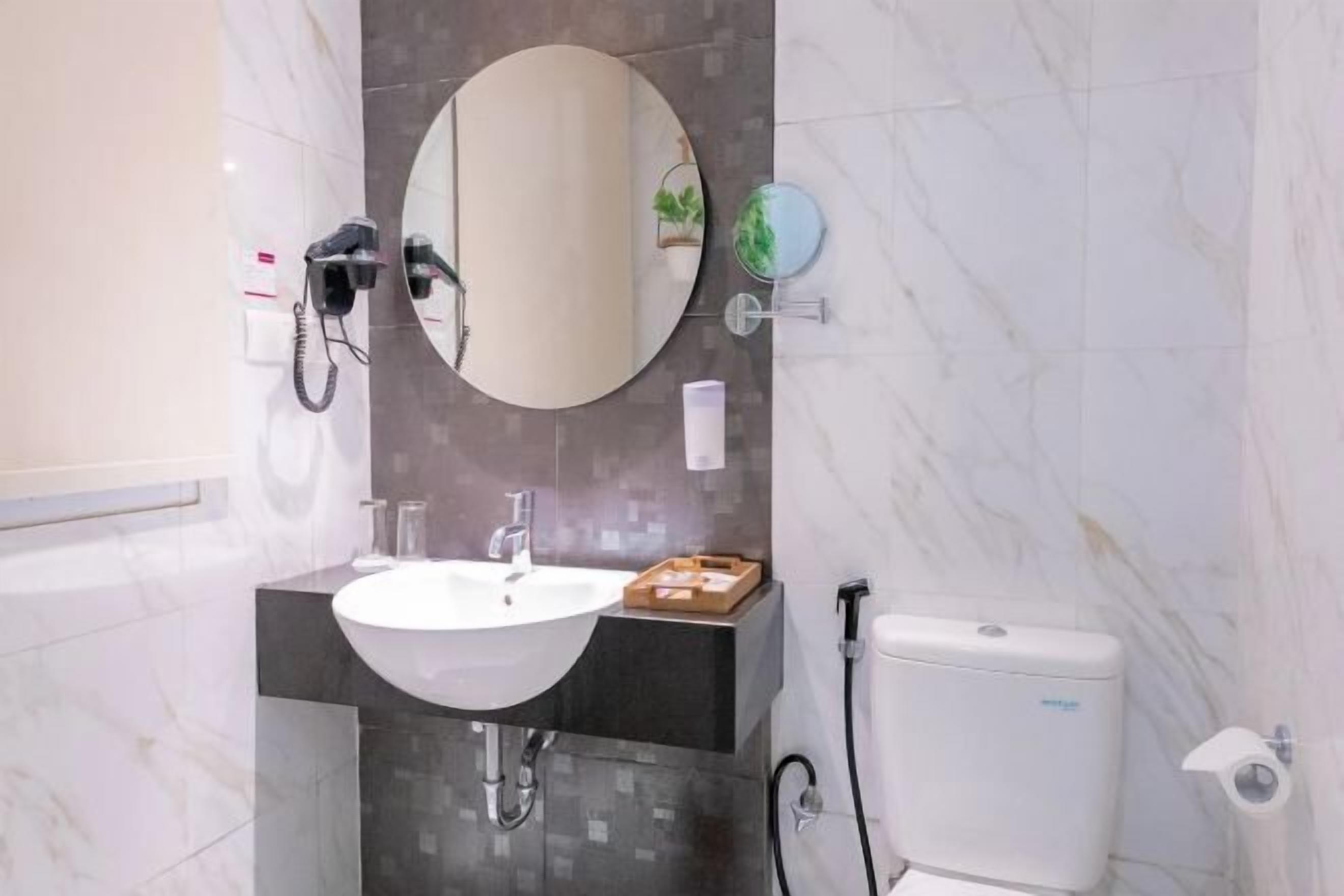 Ein Badezimmer mit einem weißen Waschbecken, einem runden Spiegel, einer Toilette und einem Fön an der Wand.