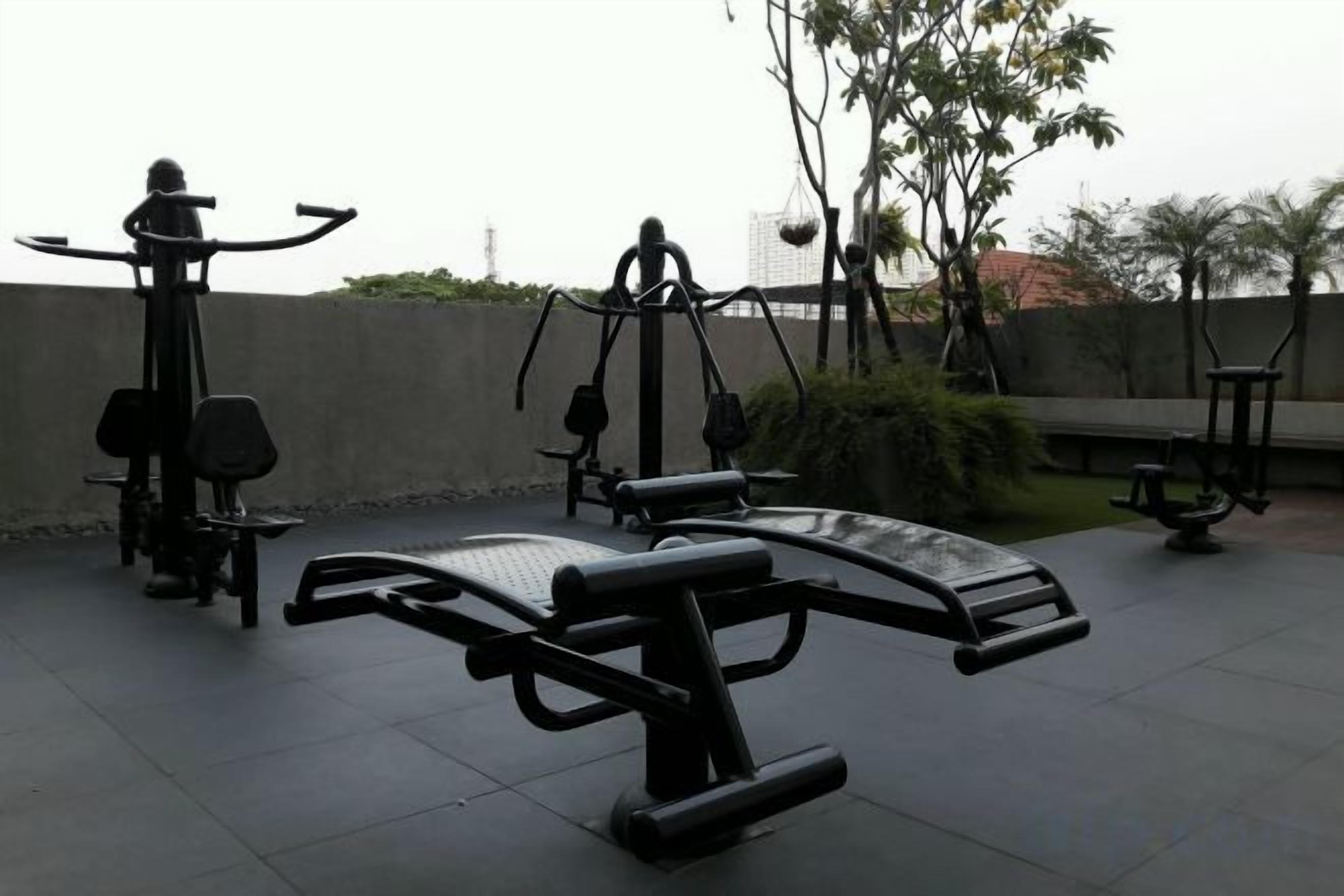 Outdoor exercise equipment, including a bench and a leg press machine, in a park setting.