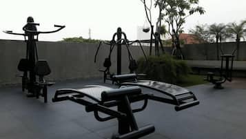 Outdoor exercise equipment, including a bench and a leg press machine, in a park setting.