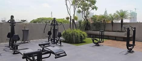 Un espace de remise en forme en plein air équipé d’appareils d’exercice, d’un banc et d’un petit jardin agrémenté d’arbres et d’arbustes.