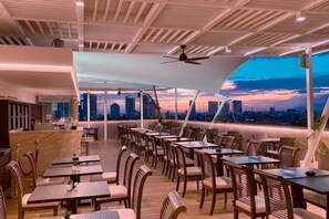 Un restaurante con mesas al aire libre, vistas al horizonte urbano y una decoración interior moderna.