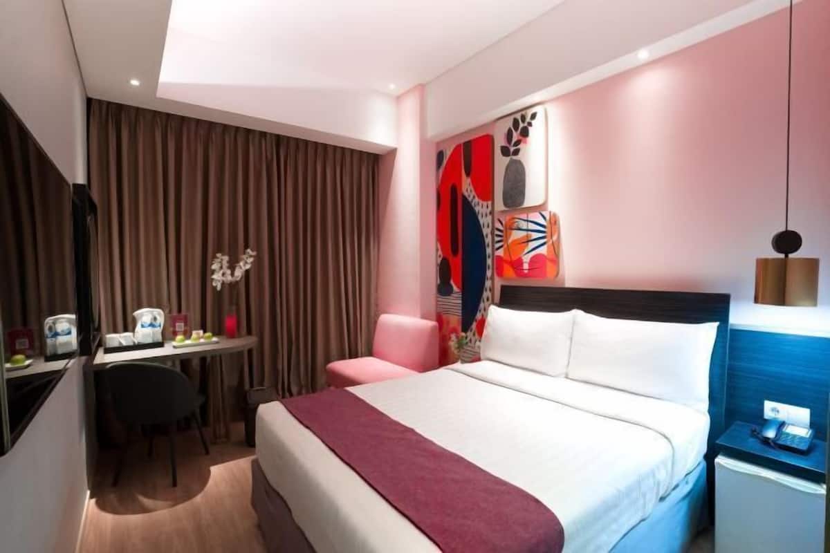 Een hotelkamer met een bed, bureau, stoel en een muur met abstracte kunst.