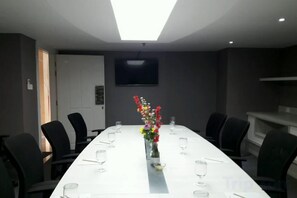 A conference room with a long table, chairs, and a TV mounted on the wall. - Brits Hotel Puri Indah (West Jakarta)