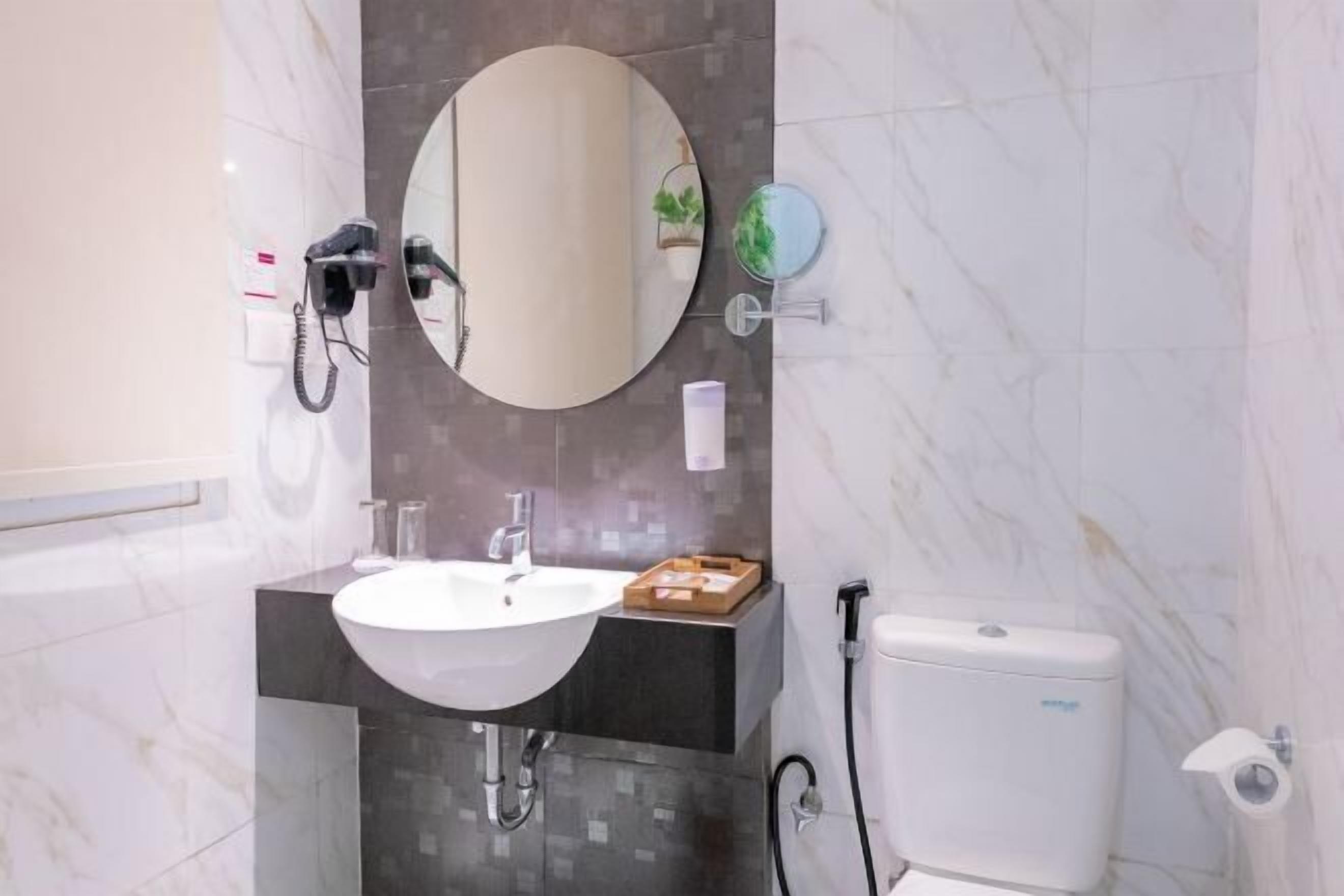 Un baño con un lavamanos blanco, un espejo redondo, un secador de pelo portátil y un inodoro.