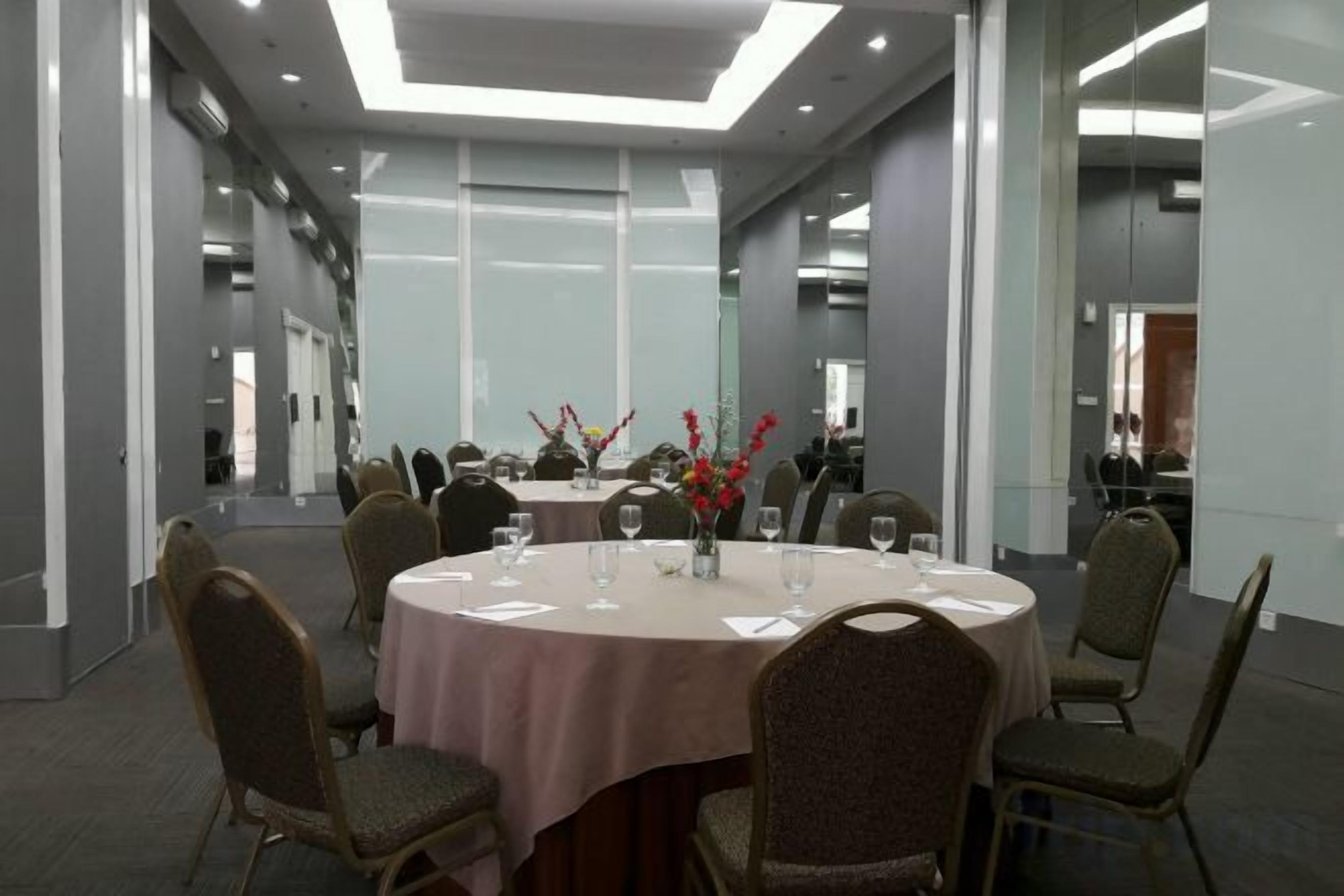 Un salón de conferencias con mesas redondas, sillas y un muro divisorio de cristal.