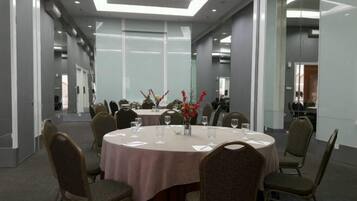 Un salón de conferencias con mesas redondas, sillas y un muro divisorio de cristal.