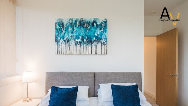 Une chambre d’hôtel avec un lit, deux oreillers, une table de chevet avec une lampe et un tableau au mur.
