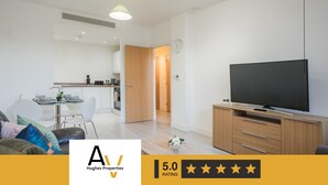 Un appartement moderne comprenant un espace de vie, une cuisine et un coin repas. Il est équipé d’un téléviseur à écran plat, de meubles en bois et d’une petite table à manger.