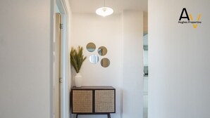 Un couloir avec une console en rotin, un vase blanc contenant des plantes et trois miroirs ronds accrochés au mur.