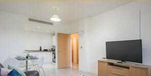 A modern apartment with a living area, kitchen, and dining space. It includes a flat-screen TV, wooden furniture, and a small dining table. - Modern 2-Bed Apartment: Your Central Getaway (Milton Keynes)