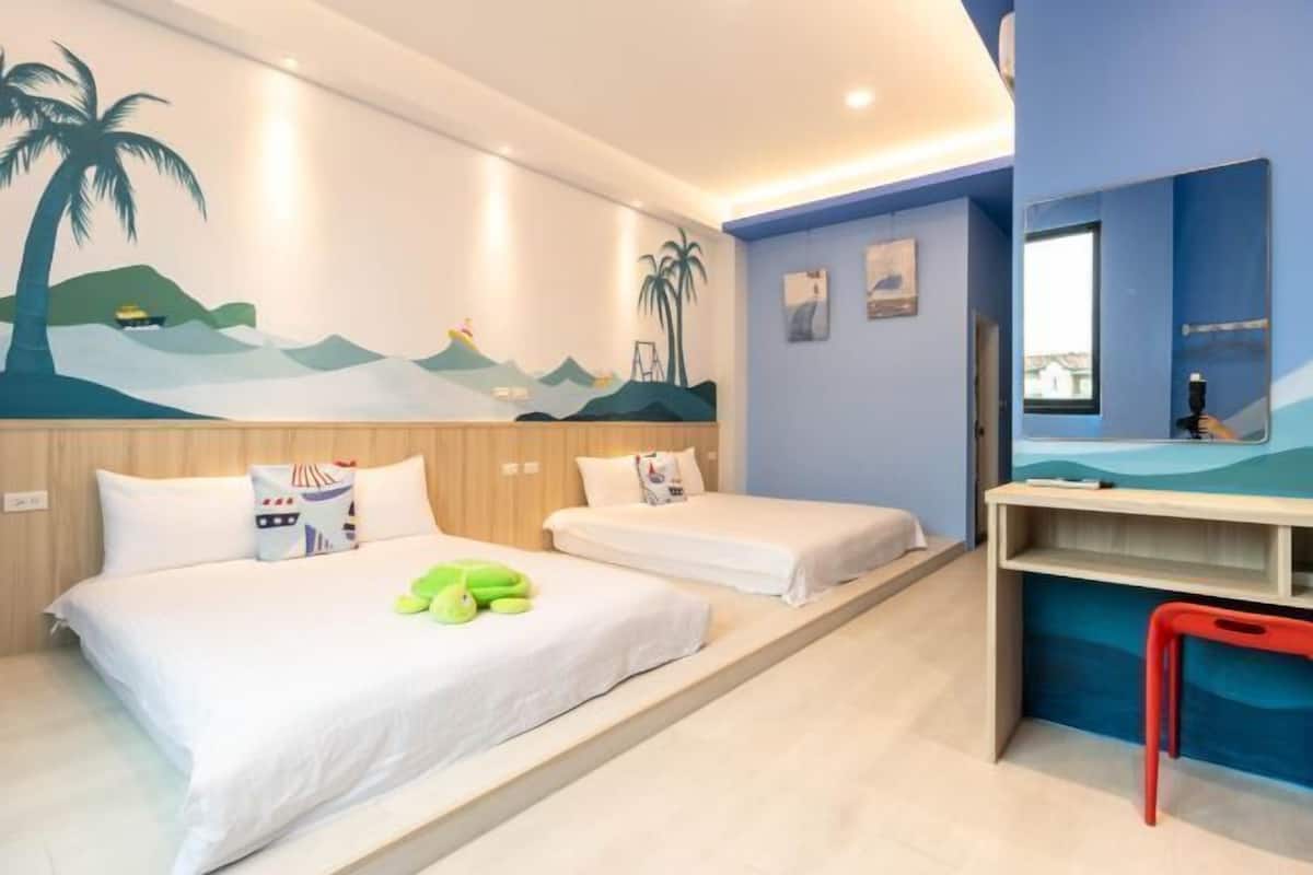 A hotel room with two beds, a desk, and a mural on the wall.