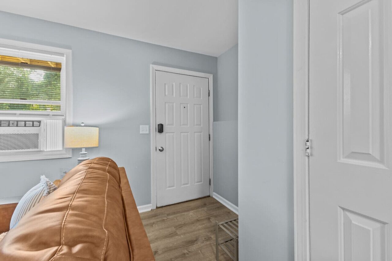 Una habitación con un sofá de cuero marrón, una puerta blanca y una ventana con persianas.