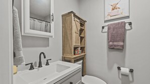 A bathroom with a white sink, a wooden cabinet, a toilet, and a framed picture on the wall.