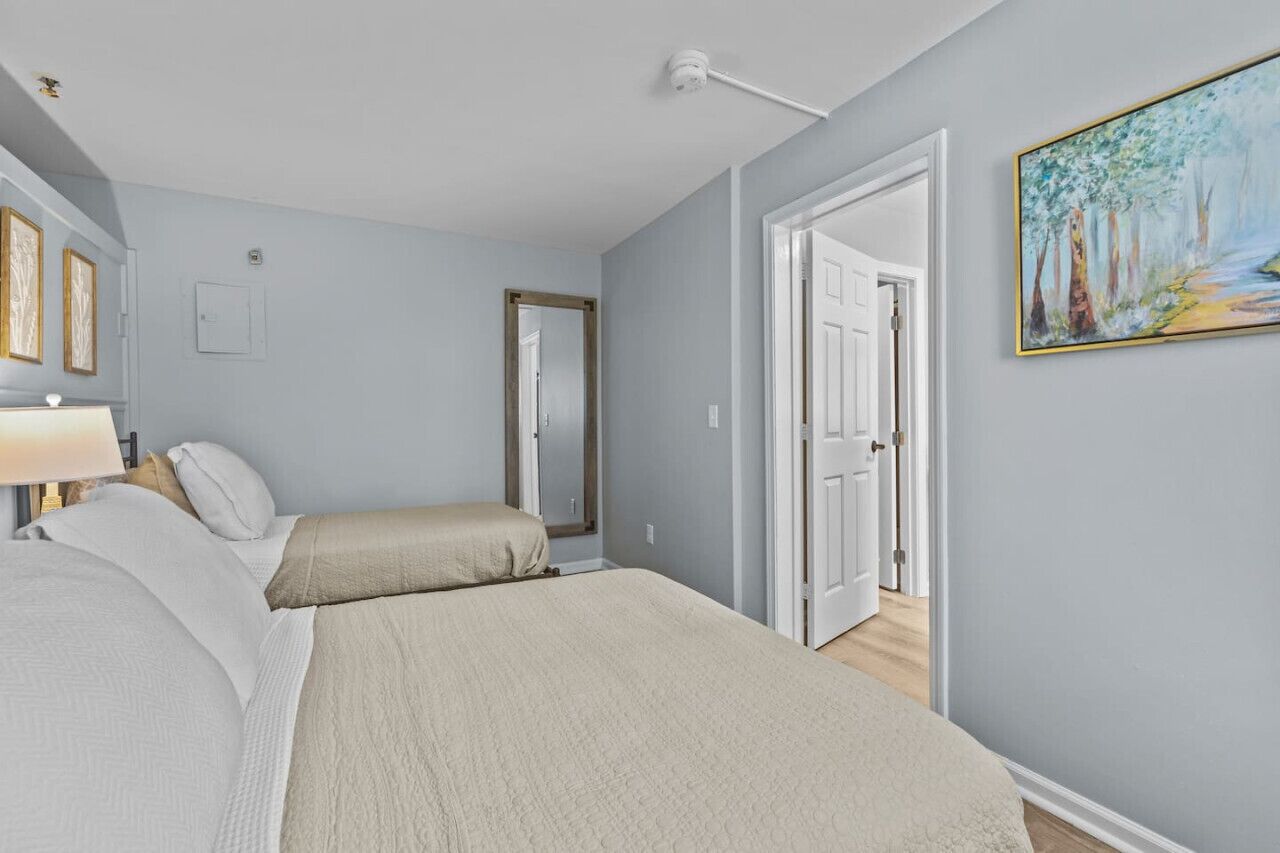 Un dormitorio con dos camas, un cuadro y una puerta que da a otra habitación.