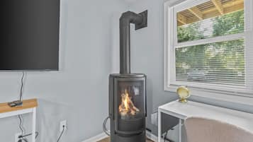 A room with a wood-burning stove, a TV mounted on the wall, a window with blinds, and a small table with a globe.