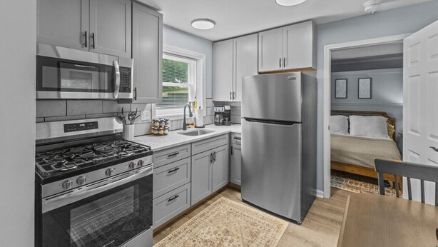 A modern kitchen with stainless steel appliances, grey cabinetry, and a window providing natural light.