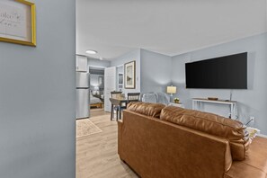 Una sala moderna con un sofá de cuero marrón, un televisor de pantalla plana en la pared y un comedor al fondo.