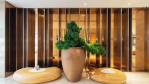A reception area with a large terracotta planter with a green topiary, two wooden stools, and a modern wooden panel wall. - JI Hotel (Xiamen Airport Huli Avenue) (Xiamen)