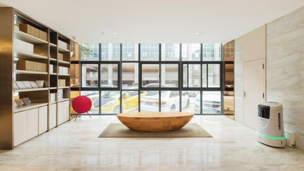 A modern interior with a central wooden table, a red chair, and a robotic vacuum cleaner. - JI Hotel (Xiamen Airport Huli Avenue) (Xiamen)