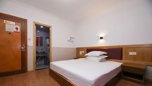 A bedroom with a wooden bed, a nightstand, a wall-mounted light, and a door with a sign. - Ala Hotel (Ningbo)