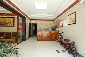 A hotel reception area with a reception desk, a sofa, a motorcycle, and a plant. - Ala Hotel (Ningbo)