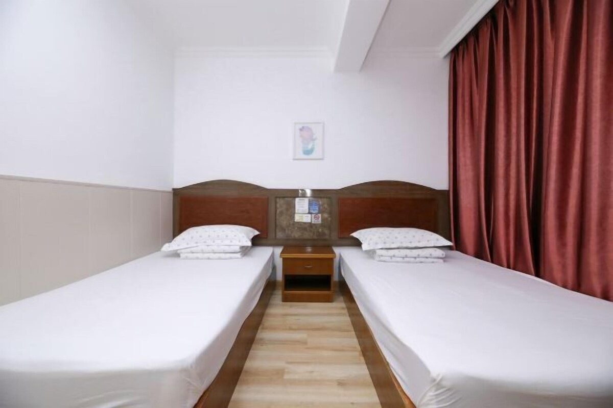 Une chambre d’hôtel avec deux lits simples, une table de chevet en bois, une petite table et un rideau rouge.