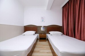 Une chambre d’hôtel avec deux lits simples, une table de chevet en bois, une petite table et un rideau rouge.