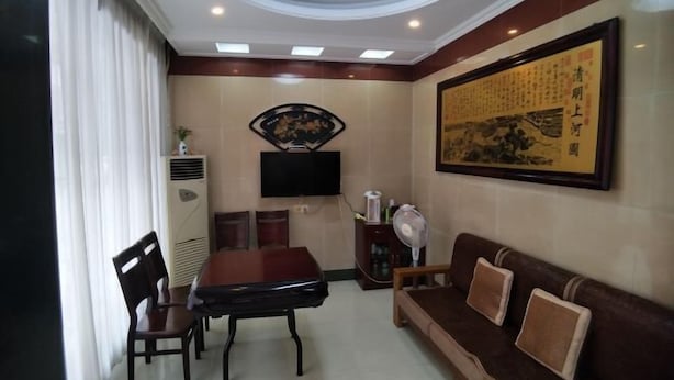 A hotel room with a dining area, a sofa, a TV mounted on the wall, and a large framed artwork. - Ala Hotel (Ningbo)