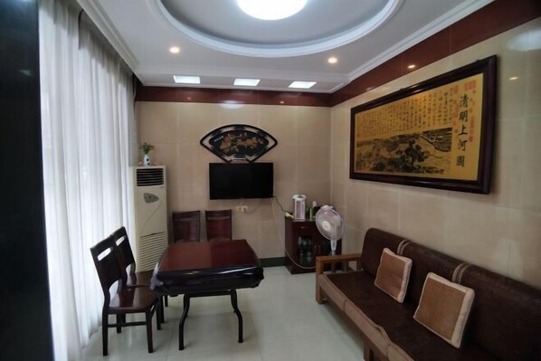 A hotel room with a dining area, a sofa, a TV mounted on the wall, and a large framed artwork.