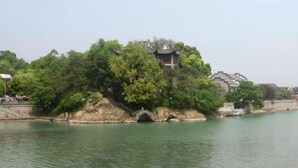 A traditional Chinese pavilion on a riverbank, surrounded by lush greenery and a stone bridge. - Ala Hotel (Ningbo)