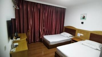 Habitación de hotel con dos camas, un escritorio de madera, una silla, un televisor y una cortina.