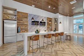 A modern kitchen with a wooden accent wall, a stainless steel refrigerator, and a bar area with stools. - Edgewater 2BR | Pool + Free Parking (Miami)