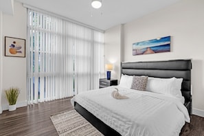 Habitación de hotel moderna con una cama grande, una mesita de noche, una lámpara, un cuadro y vistas a través de cortinas translúcidas.