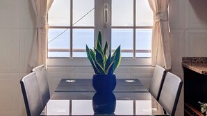 A dining area with a table and chairs, a potted plant, and a view of the sea through a window with curtains. - Ocean Serenity House by Atlantic Holiday (Ribeira Brava)