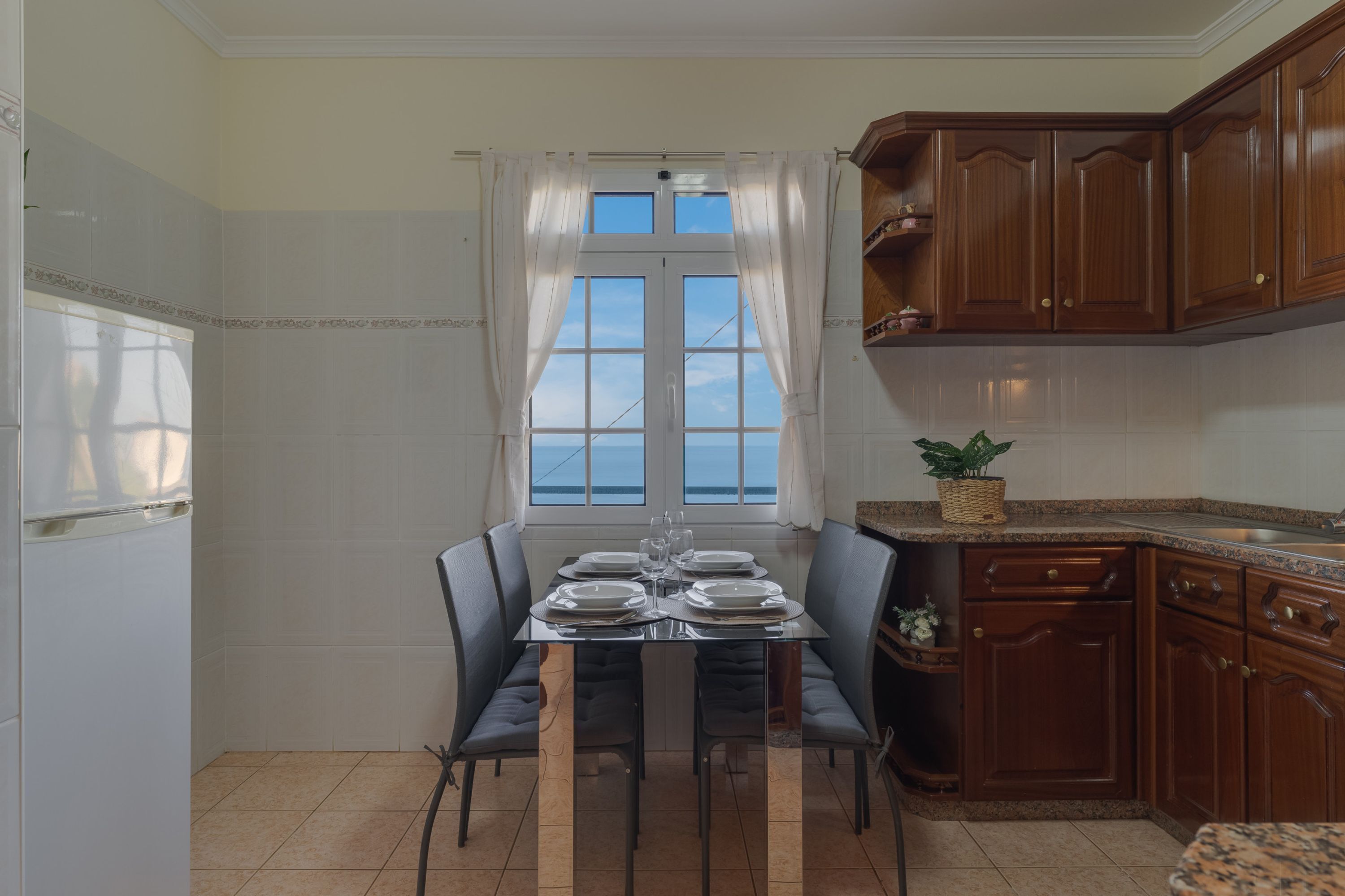 A dining area with a table set for four, a window with curtains, and wooden cabinets.
