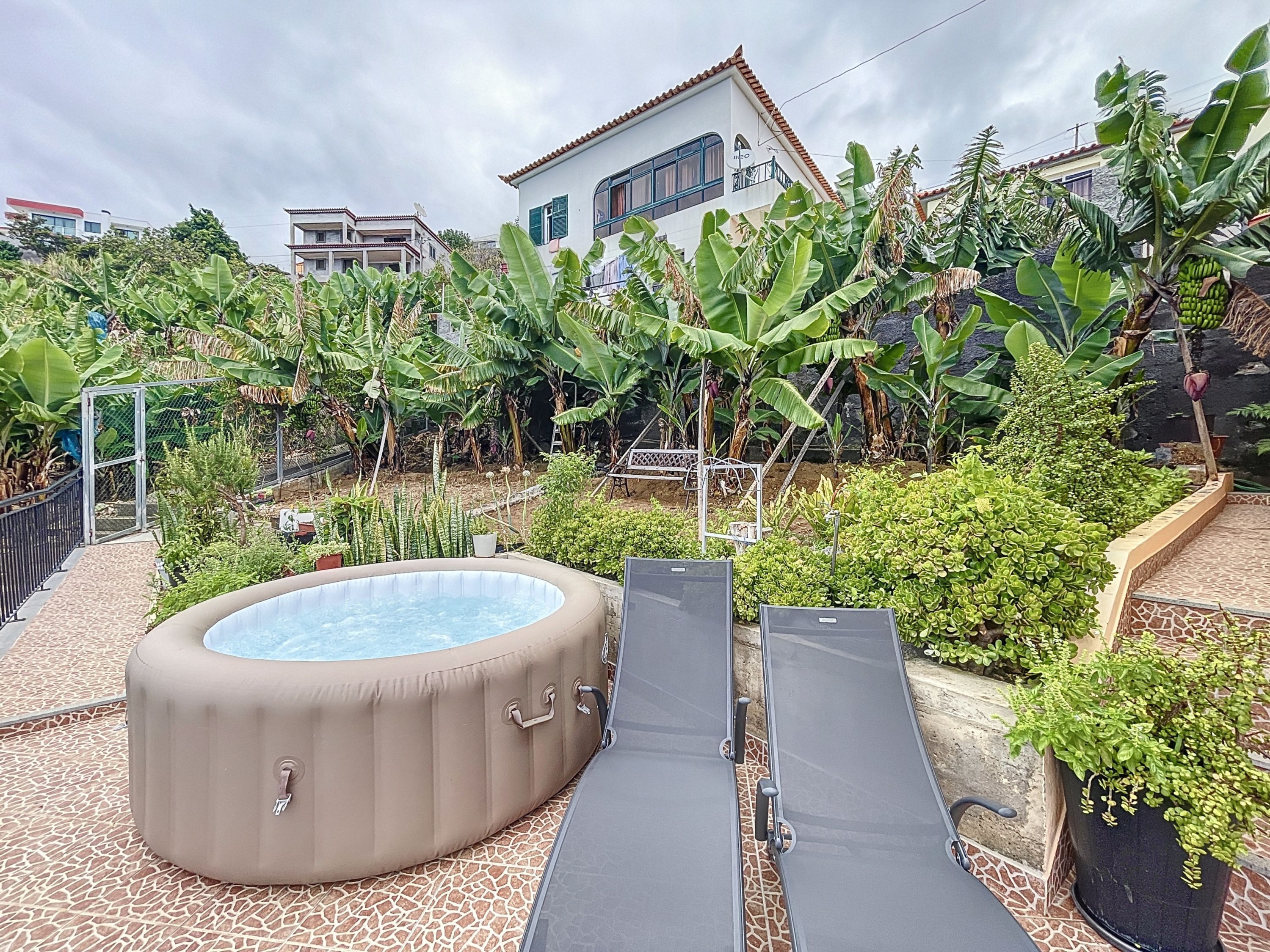 A hot tub with a pool, surrounded by lush greenery and a tiled patio.