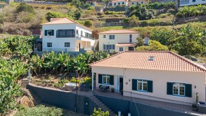 A residential area with houses on a hillside, featuring a two-story building with a balcony and a patio area with outdoor furniture. - Ocean Serenity House by Atlantic Holiday (Ribeira Brava)