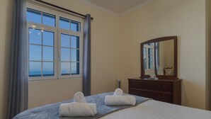 A hotel room with a bed, a dresser, a mirror, and a window with curtains. - Ocean Serenity House by Atlantic Holiday (Ribeira Brava)