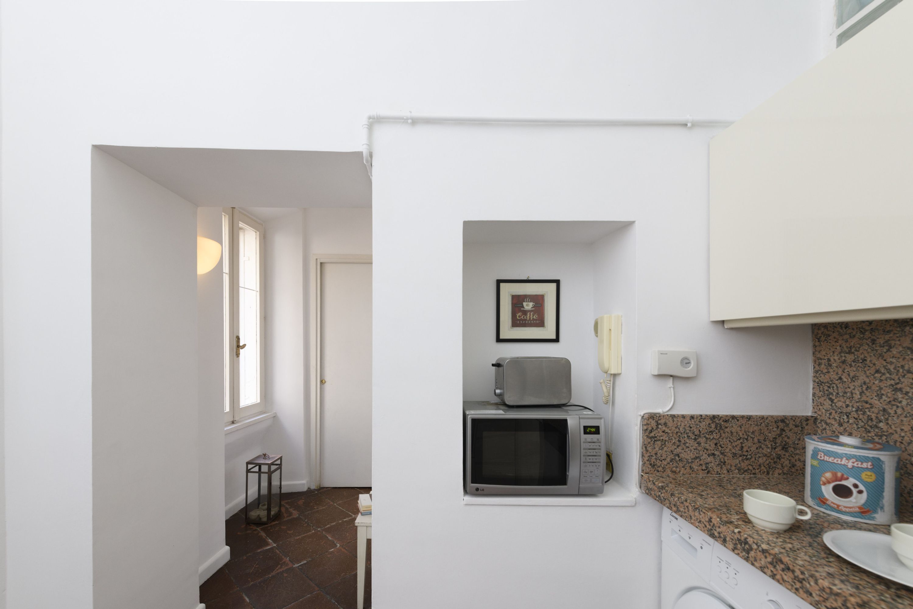 A compact kitchen with a microwave, a coffee maker, and a breakfast cereal box on the counter.