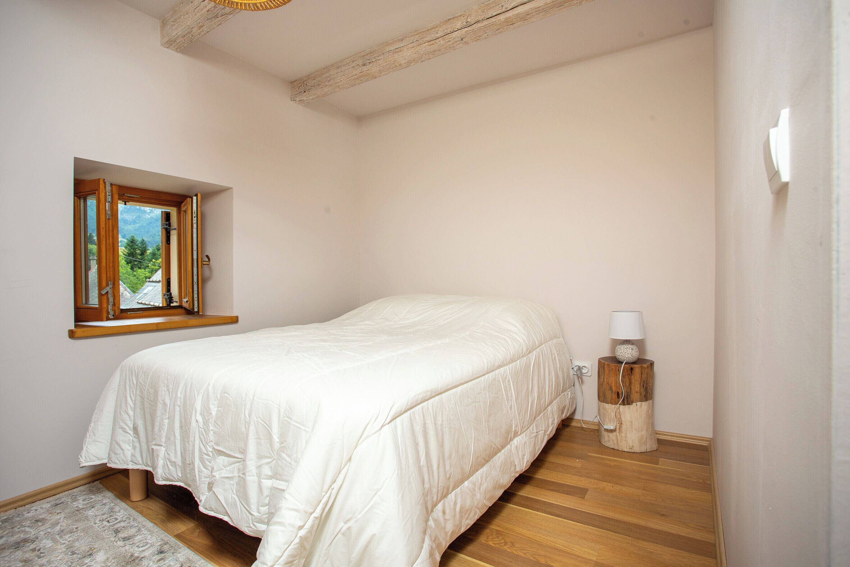 A bedroom with a bed, a window, a lamp, and a small wooden stool.