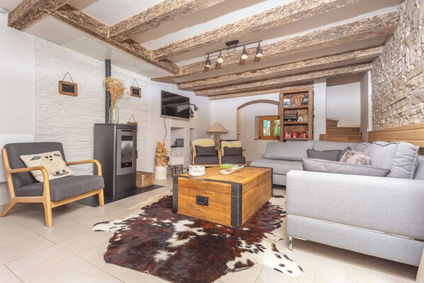 A living room with a sofa, a wooden coffee table, a leather rug, a TV, and a fireplace. - L'écrin de Brévardière (Saint-Pierre-de-Chartreuse)