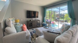Una sala de estar con un televisor grande, sofás grises y una puerta de vidrio que da a un patio al aire libre.
